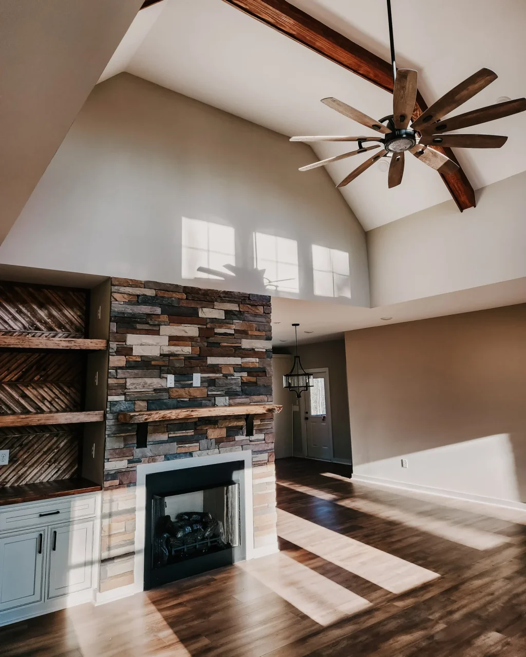 Spacious living room in Pauline country home with high ceiling, rustic stone fireplace, and wooden beams.