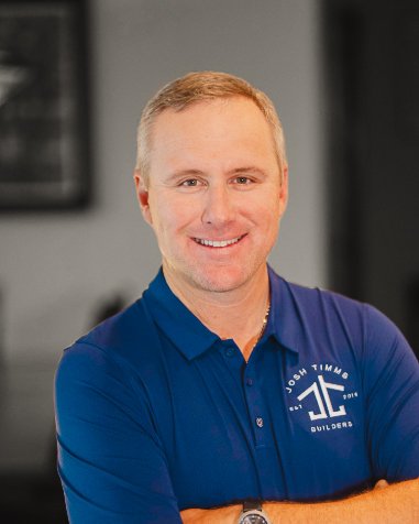 Josh Timms of Timms Builders smiling, wearing branded blue polo. Focus on custom homebuilding vision.