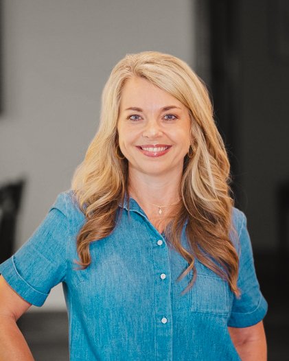 Smiling woman with long blonde hair in a denim shirt, representing Josh Timms Builders' vision of a higher standard.