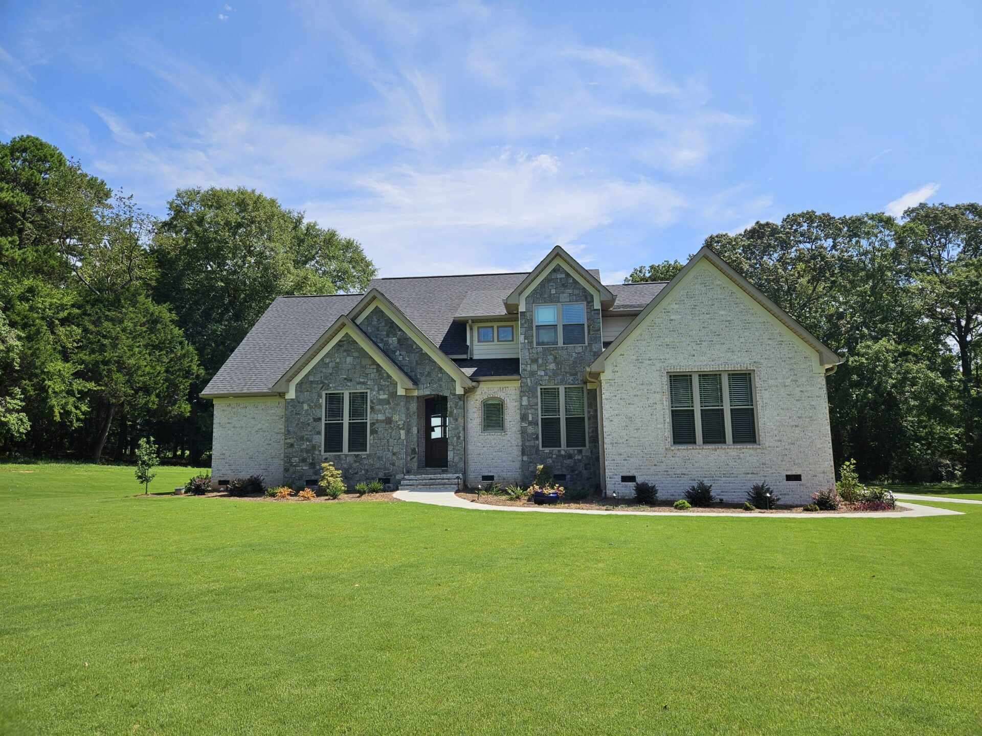 Elegant custom home with a stone facade and lush green lawn, exemplifying enjoyable home building.