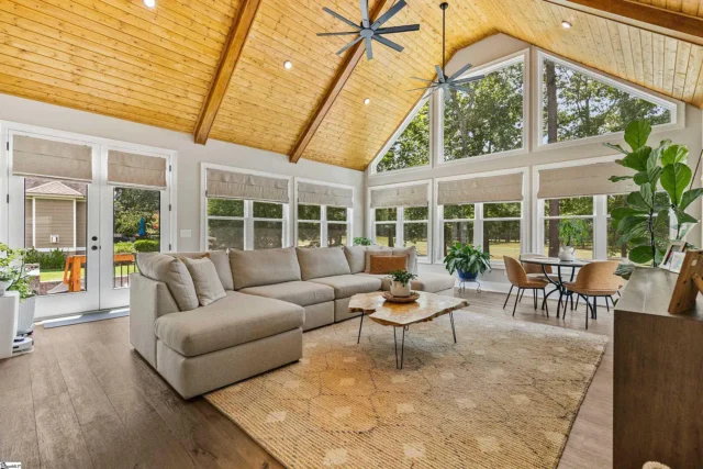 Spacious living room with vaulted wooden ceiling, large windows, beige sectional, and plants in your custom home.